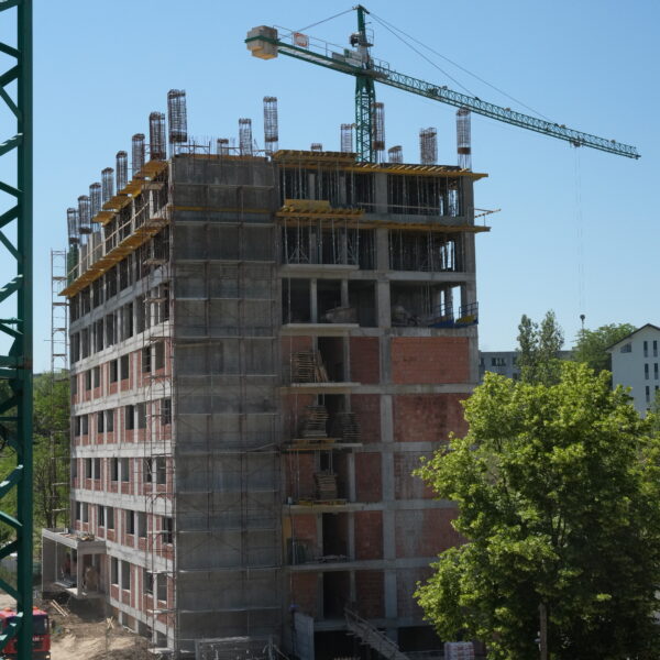 Construction site with a multi-story building under construction and a tall crane overhead, blue sky above.